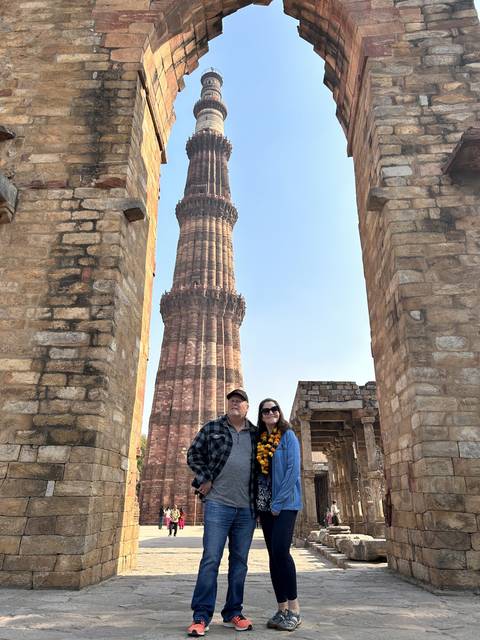       Two people posing with Qutub Minar in New Delhi.
  