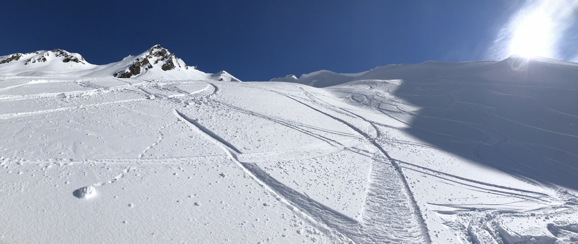 Snowy mountainside with ski tracks under a clear blue sky.