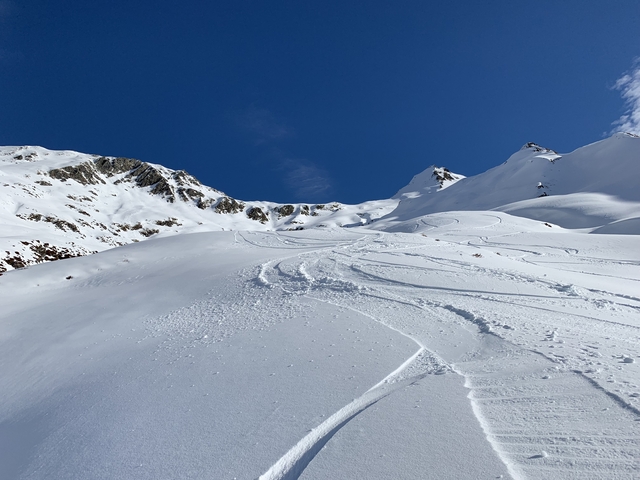 Snowy mountain with ski tracks and clear blue skies.