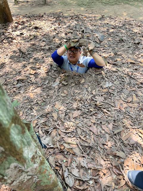 A person emerging from a leaf-covered area, camouflaged in the forest.