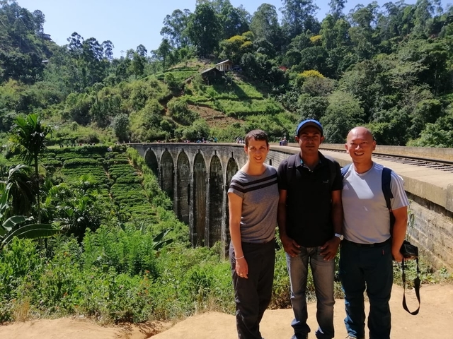       Three people posing in front of a scenic railway bridge.
  
