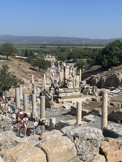       Ruins of an ancient city with columns and tourists exploring.
  