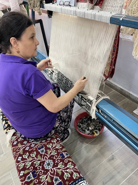       A person working on a weaving loom with colorful patterns.
  