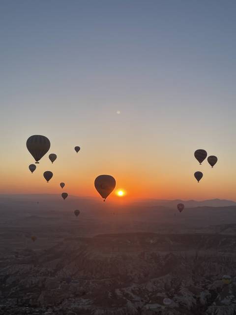       Hot air balloons at sunrise over a mountainous landscape.
  