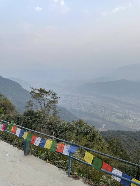       View of hills with colorful prayer flags in the foreground.
  
