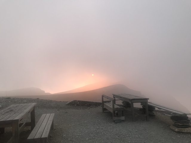 Misty sunrise over a mountainous landscape with wooden benches.