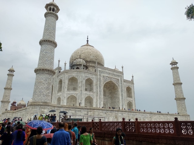 A side view of the Taj Mahal with several tourists holding umbrellas.