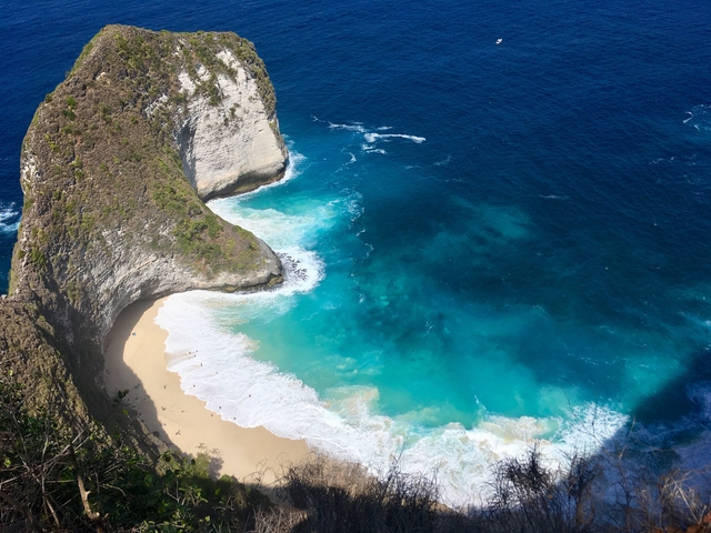       Aerial view of a beach with clear turquoise water and a dramatic cliff.
  