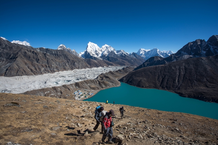       Hikers descending a mountain path with a view of a glacier and lake.
  