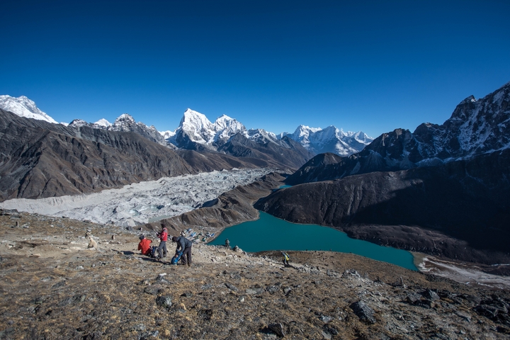       Hikers overlooking a glacier and turquoise lake in the mountains.
  