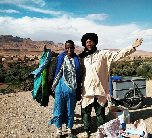       Two men in traditional attire with a desert village in the background.
  