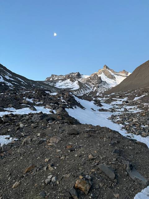 Mountainous landscape under a clear blue sky with visible moon.