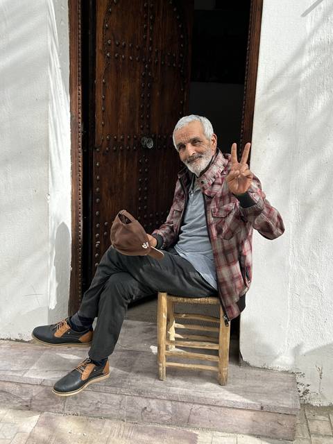       Man sitting outside a rustic wooden door.
  