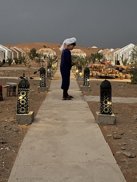       Person walking on a path with lanterns in a desert setting.
  