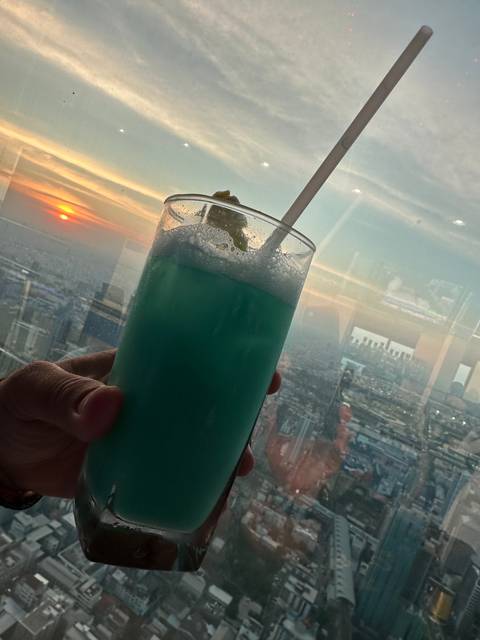 Blue cocktail with a straw being held against a sunset view.