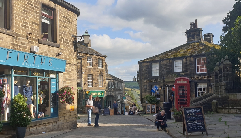 A street scene in a quaint town with stone buildings, shops, and a red phone booth.