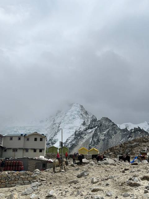 Camp at the base of a snowy mountain with clouds overhead.