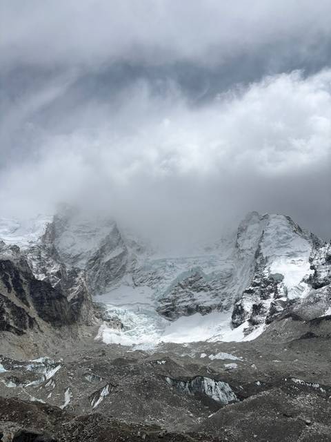 Mountain glacier with snow-capped peaks and cloudy sky.