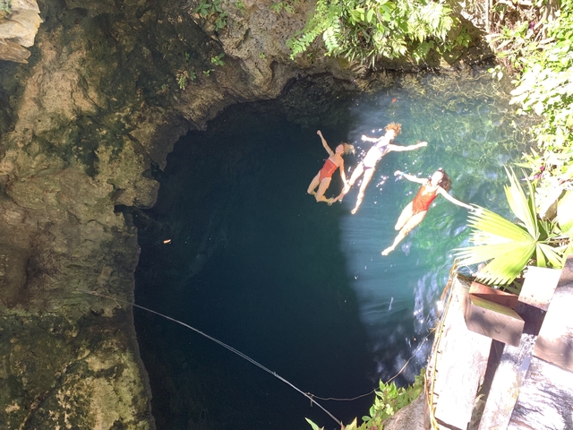 People swimming in a cenote with clear water.