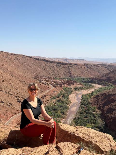       Person sitting on rocks with a large canyon and greenery in the background.
  