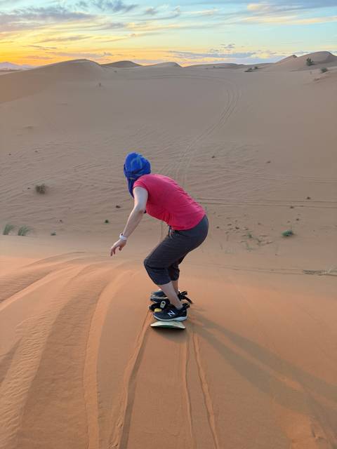 Person sliding down sand dunes, possibly sandboarding.