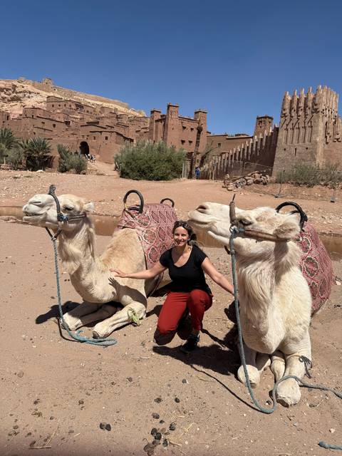       Person posing with camels near desert structures.
  