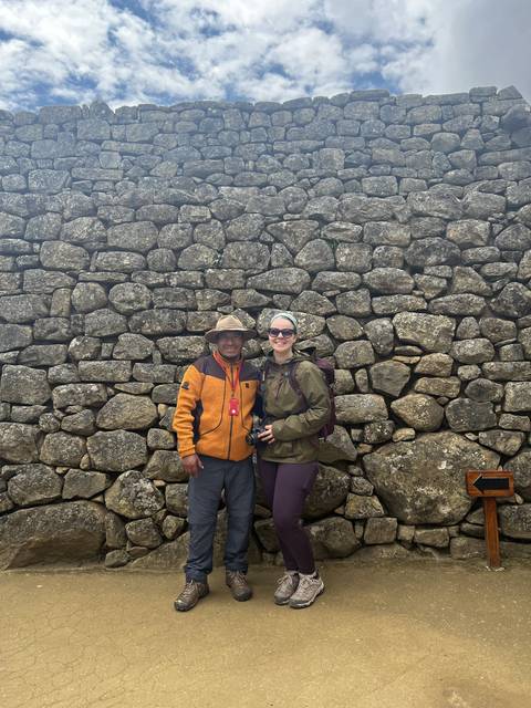 Two people posing in front of a stone wall.