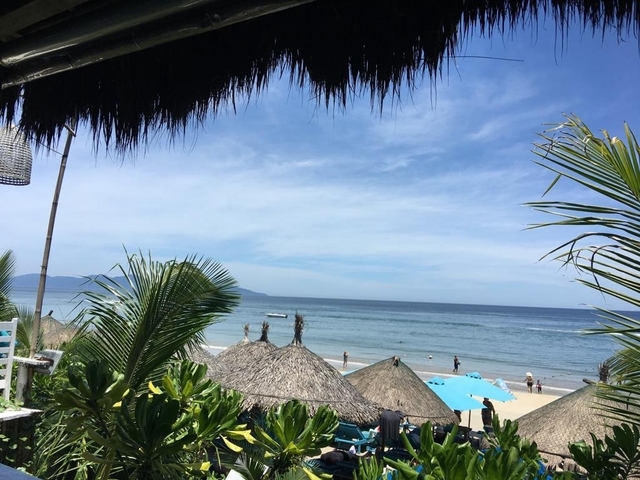 View of a beach with thatched umbrellas and distant mountains.