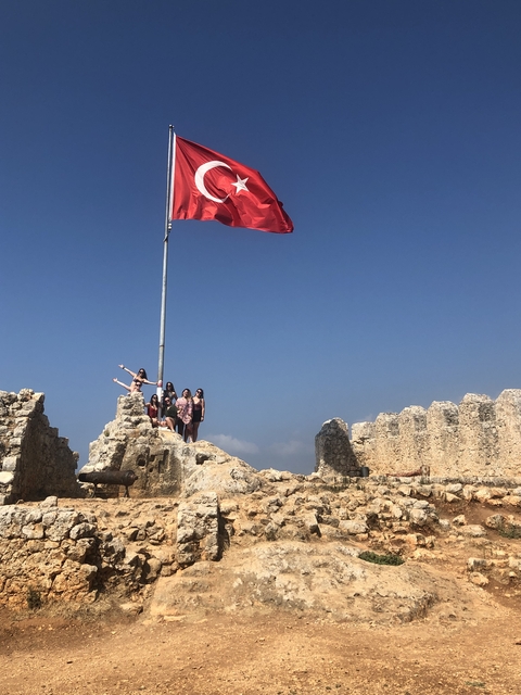       Group of people posing on ancient ruins with a flag.
  