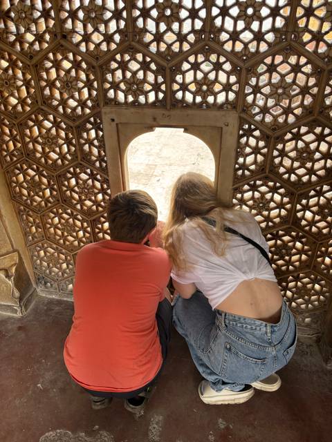 Two people looking through a window in an ornate setting.