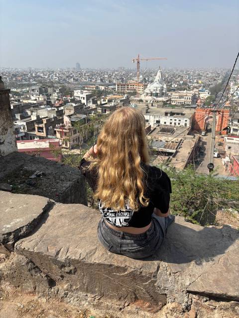       Person sitting on rocks overlooking a cityscape.
  