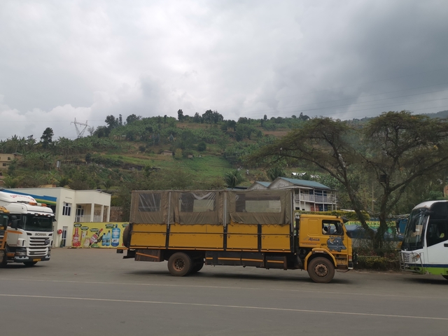 A yellow truck parked with a green hill in the background.
