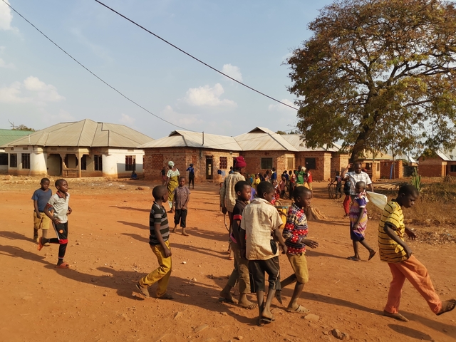 A group of children playing in a village with dirt roads.