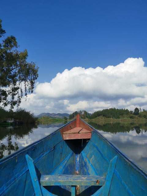 Boat on a lake with clouds and greenery in background.