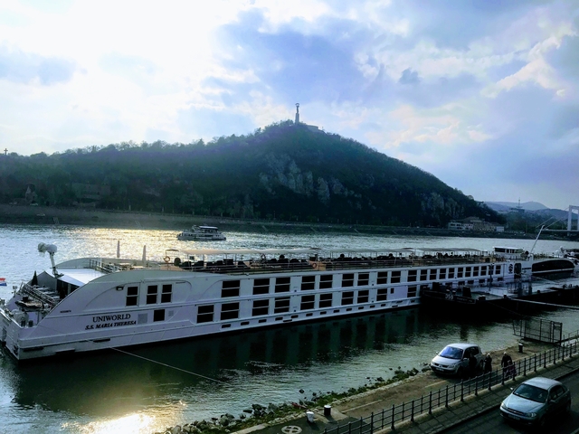 River cruise ship docked along a river with a hill in the background.