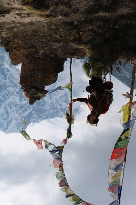 A hiker posing with prayer flags and mountains in the background.