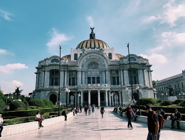 A grand building with a dome and statues in an urban park setting.