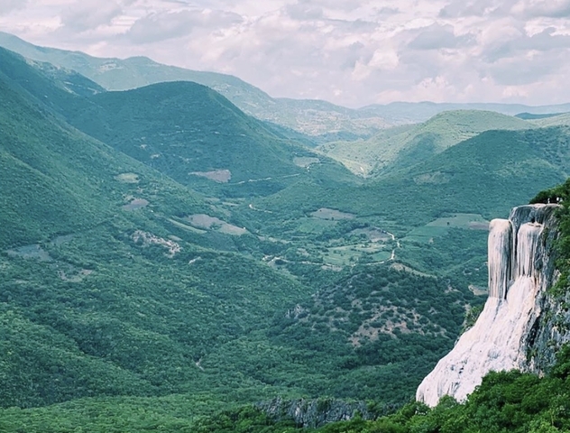 Distant shot of mountains with a bright blue sky and a waterfall to the side.
