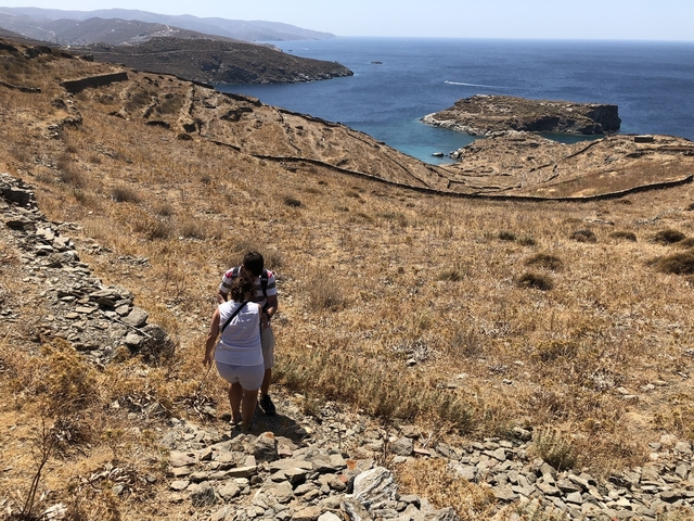 Two people hiking on a hill near the coast with a clear blue sea view.