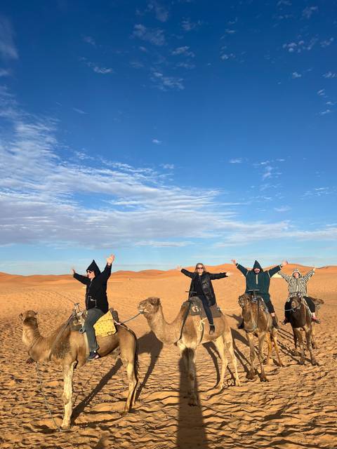       People posing with camels in the desert.
  