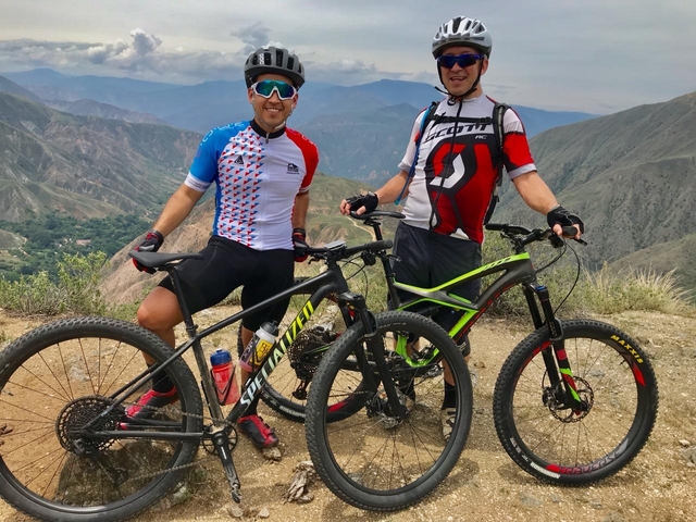 Two cyclists posing with their bikes against a hilly background.