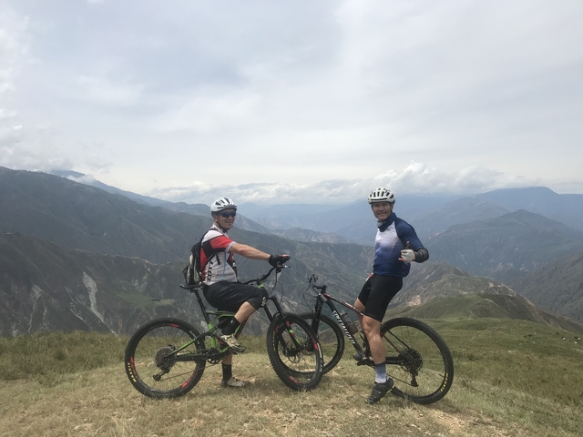 Two cyclists at a mountain peak with a vast landscape.