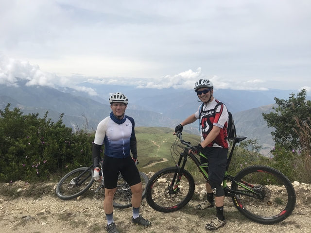 Two cyclists posing with a mountainous backdrop.