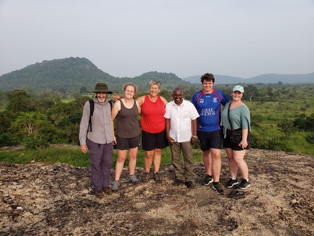 Group of six people standing on a rocky platform with a scenic backdrop.