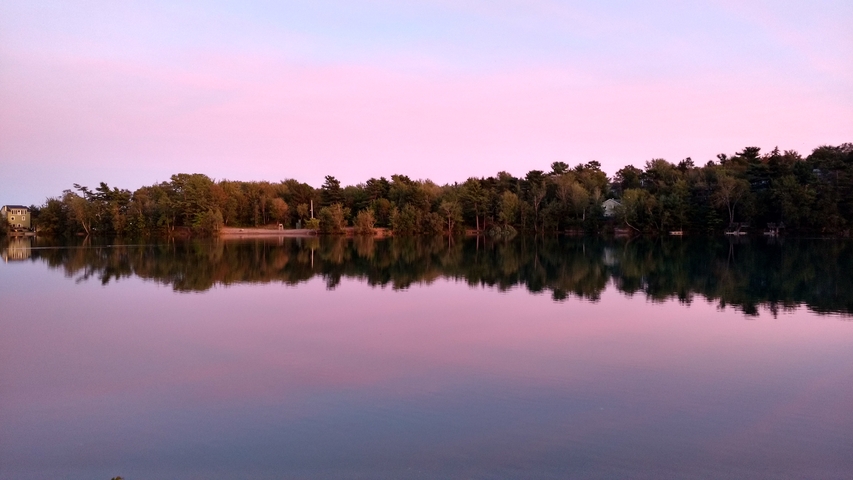       Reflection of trees on a calm lake during sunset.
  