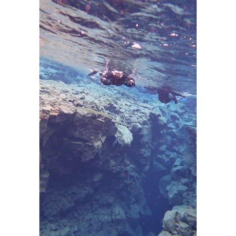 People snorkeling in clear blue waters over rocky terrain.