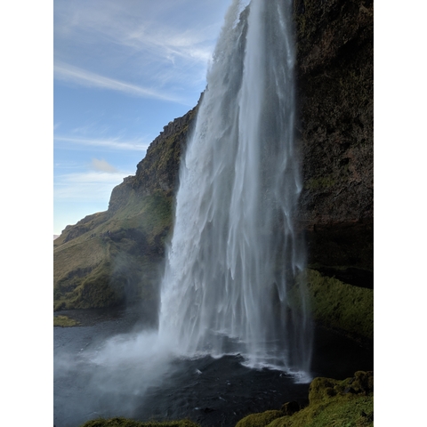 Tall waterfall dropping from a cliff with blue sky.