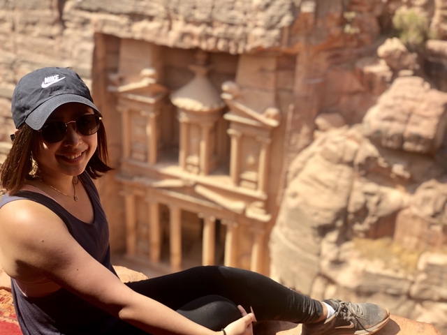       A woman posing on a cliff with the iconic Petra Treasury visible in the background.
  