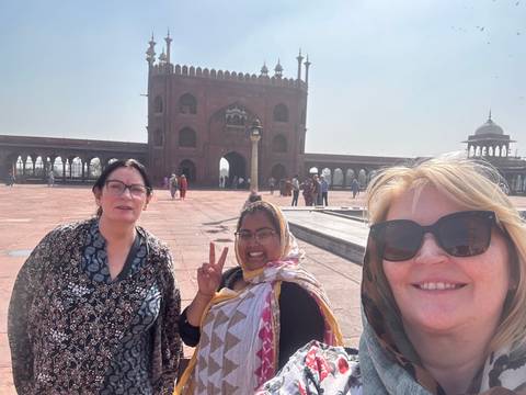 Three women posing in front of an upside-down architectural structure.