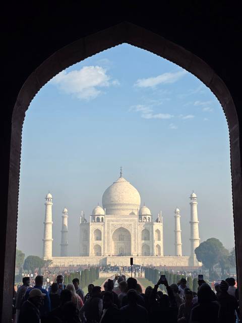 Taj Mahal viewed through an archway, crowded with visitors.